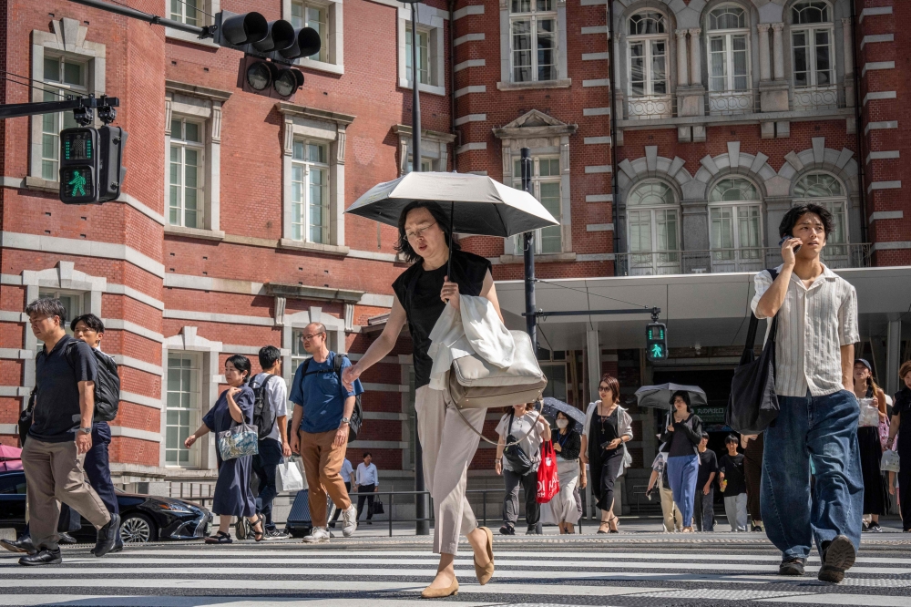 People cross a street outside Tokyo Station on a hot day in Tokyo on August 27, 2025. (Photo by Yuichi Yamazaki / AFP)
