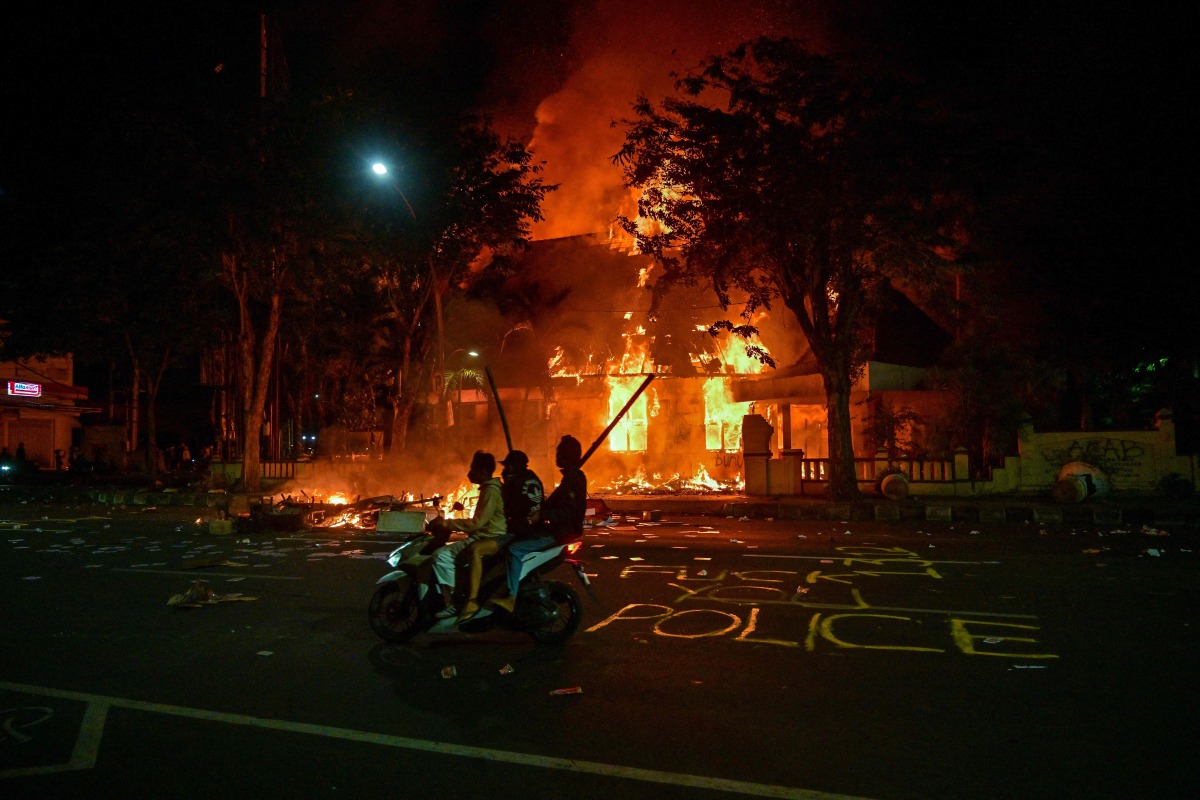 Protesters rides a motorcycle in front of a police headquarters that was burned and looted during demonstrations in Surabaya on August 31, 2025. Photo by Juni KRISWANTO / AFP