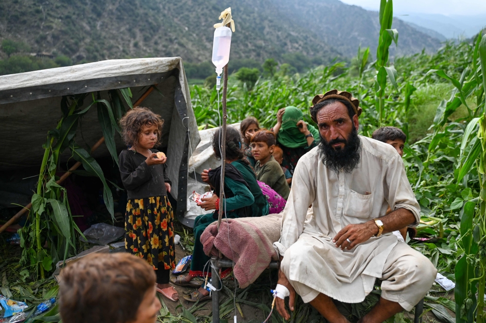 An Afghan injured man receives intravenous drips in a corn field, after earthquakes at Mazar Dara village in Nurgal district, Kunar province, in Eastern Afghanistan, on September 1, 2025. (Photo by Wakil Kohsar / AFP)