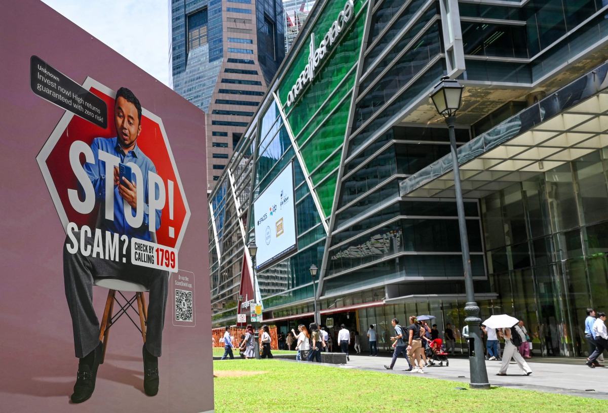 People walk past a poster warning of scam threats in the financial business district of Raffles Place in Singapore on September 3, 2025. Photo by Roslan RAHMAN / AFP