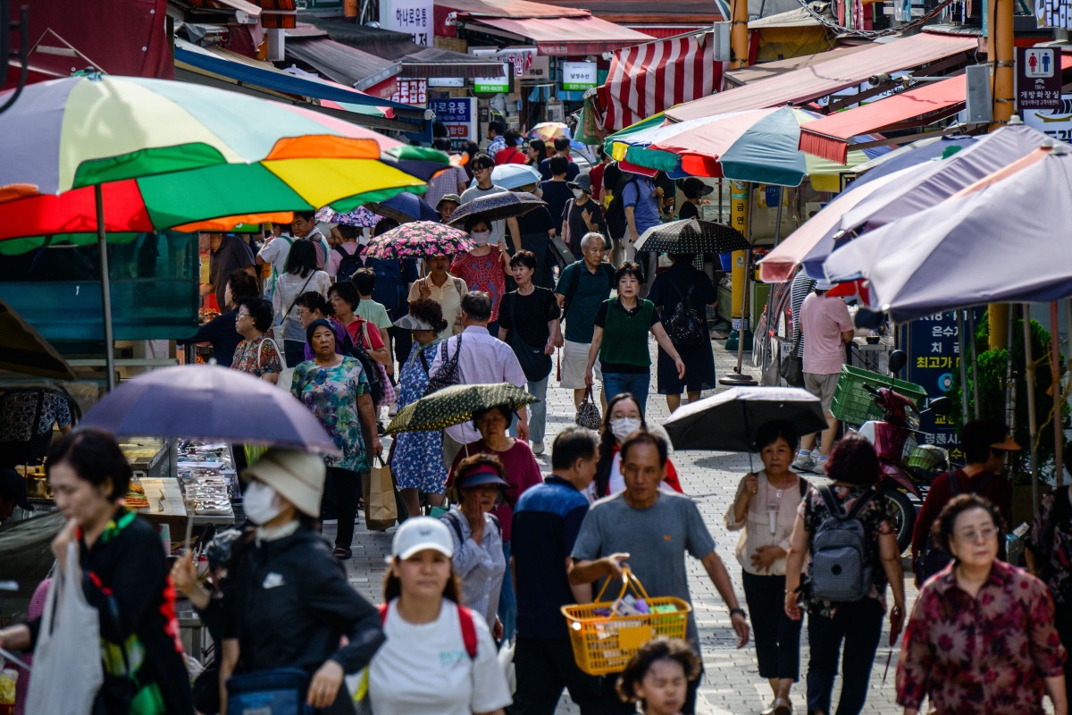 People walk past stalls at a street market in Seoul on September 3, 2025. (Photo by ANTHONY WALLACE / AFP)
