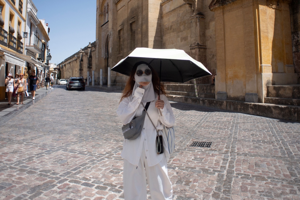 A tourist protects from the sun with a mask and an umbrella during a heatwave in Cordoba, in southern Andalusia region, in Spain, on August 3, 2025. (Photo by Jorge Gurrrero / AFP)
