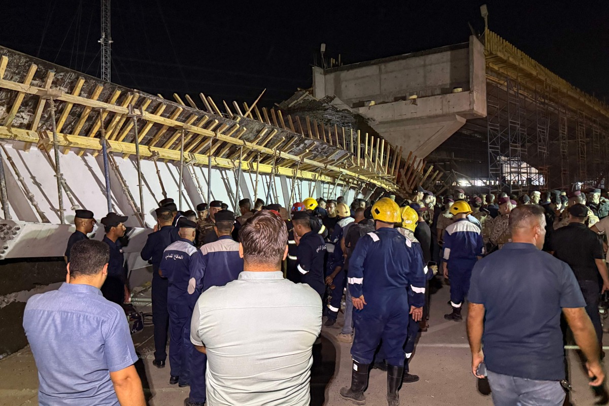 First responders and onlookers gather in front of a bridge under construction, after a section of it collapsed, killing two people and injuring others, in Karbala in southern Iraq late on September 6, 2025. Photo by Salman AMIN / AFP