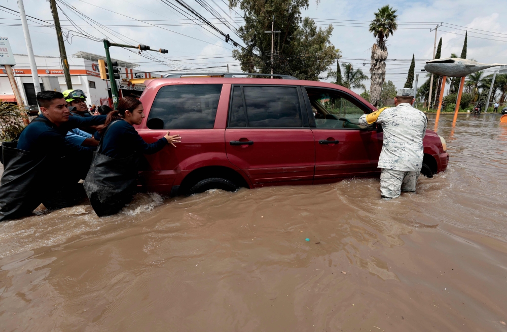 Firefighters and a member of the National Guard assist a driver stranded in floodwater after heavy rains caused the Arroyo Seco River to overflow in Tlajomulco de Zٌْiga, Jalisco, Mexico, on September 9, 2025. (Photo by ULISES RUIZ / AFP)
