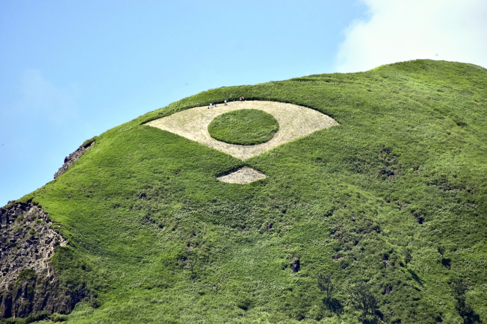 Grass mowed into the shape of a fan bearing the Japanese flag is seen on a mountain in Aso, Kumamoto Prefecture. Photo by The Japan News
