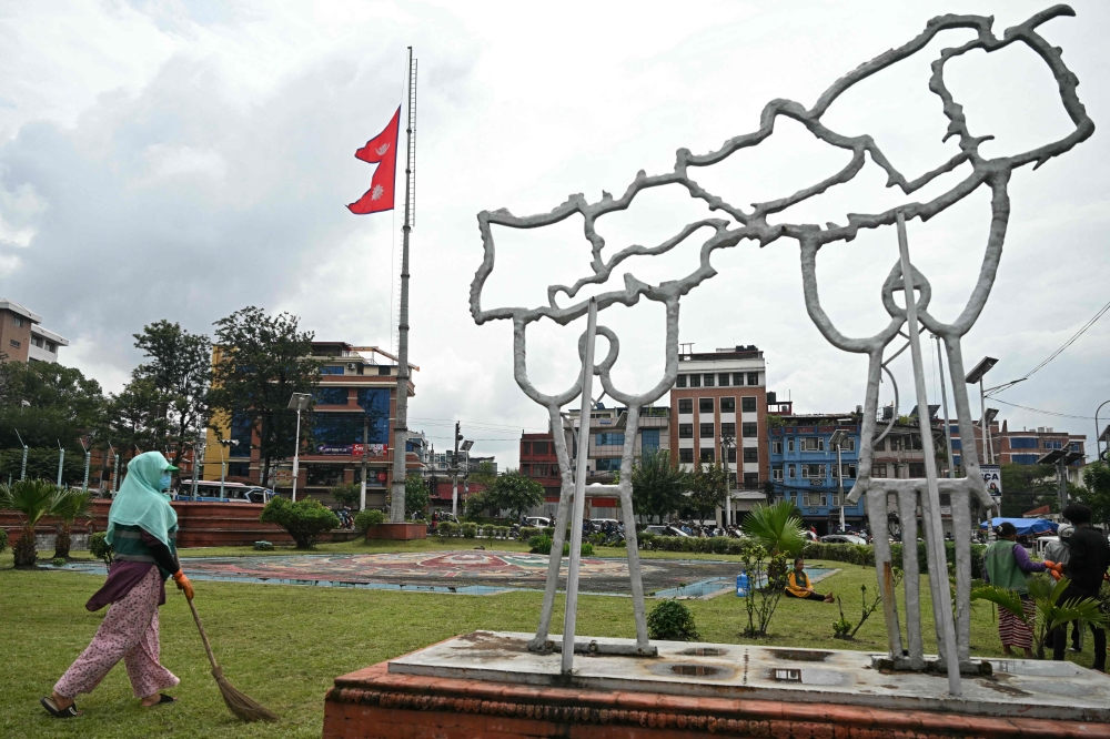 A civic worker walks past Nepal's national flag flying at half-mast next to a structure built in the shape of country's map, in Kathmandu on September 17, 2025. (Photo by Arun Sankar / AFP)