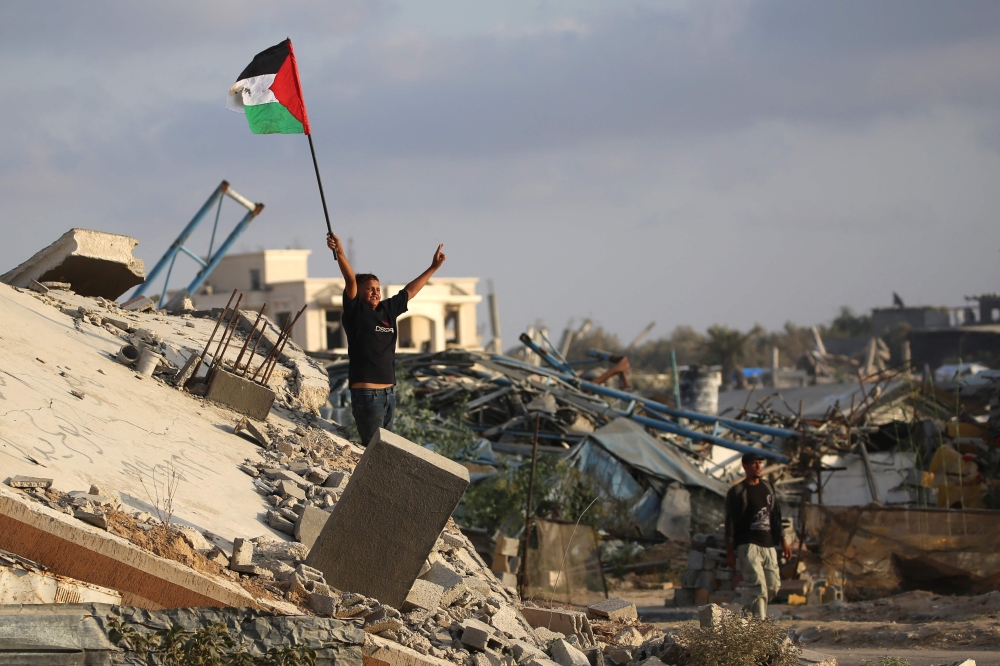 A displaced Palestinian child waves a Palestinian national flag as he stands on the rubble of a destroyed building at the Bureij camp for refugees in the central Gaza Strip on September 22, 2025. (Photo by Eyad Baba / AFP)