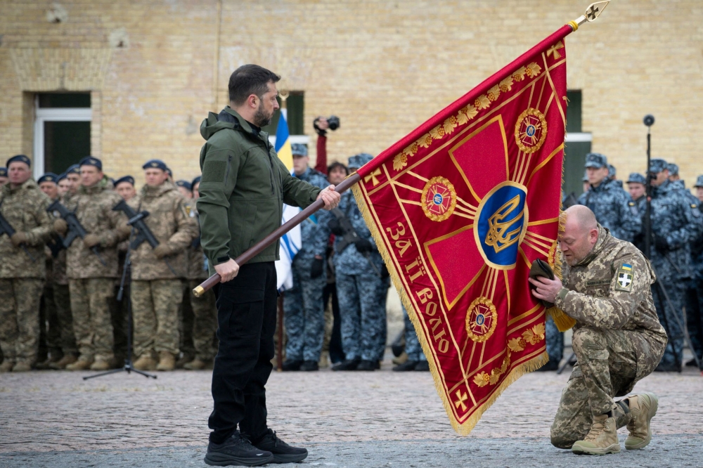 This handout photograph taken and released by the Ukrainian Presidential Press Service on October 1, 2025, shows Ukraine's President Volodymyr Zelensky holding a flag insignia as a serviceman pays his respect during a ceremony marking Defenders' Day, a holiday honoring veterans and fallen members of the Ukrainian armed forces. (Photo by Handout  / AFP)