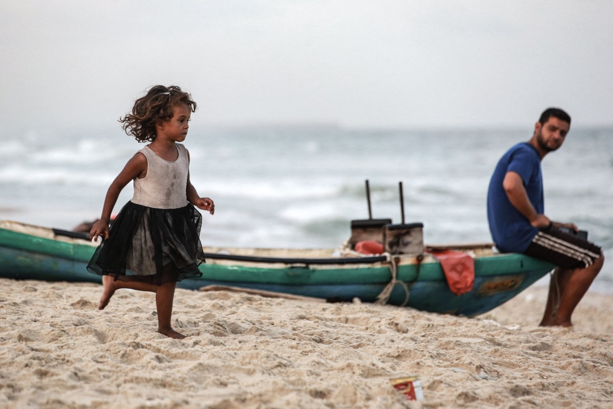 A displaced Palestinian girl runs along the beach as a man sits on a fishing boat, in Deir el-Balah in the central Gaza Strip, on October 5, 2025. (Photo by Bashar TALEB / AFP)

