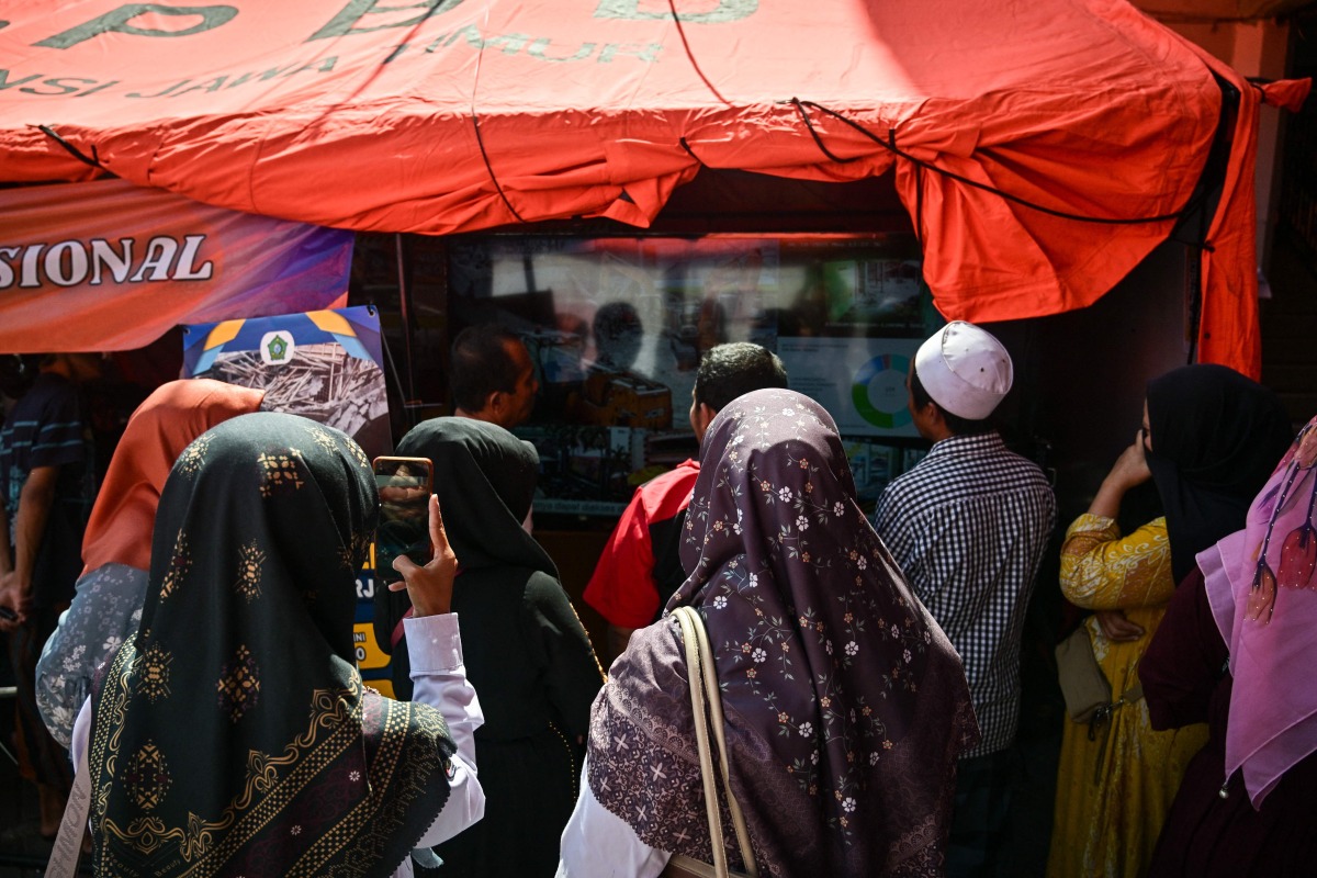 Relatives of missing students watch a live broadcast of the rescue operation near the collapsed Al Khoziny Islamic boarding school in Sidoarjo, East Java, on October 6, 2025, as recovery efforts continue. Photo by JUNI KRISWANTO / AFP