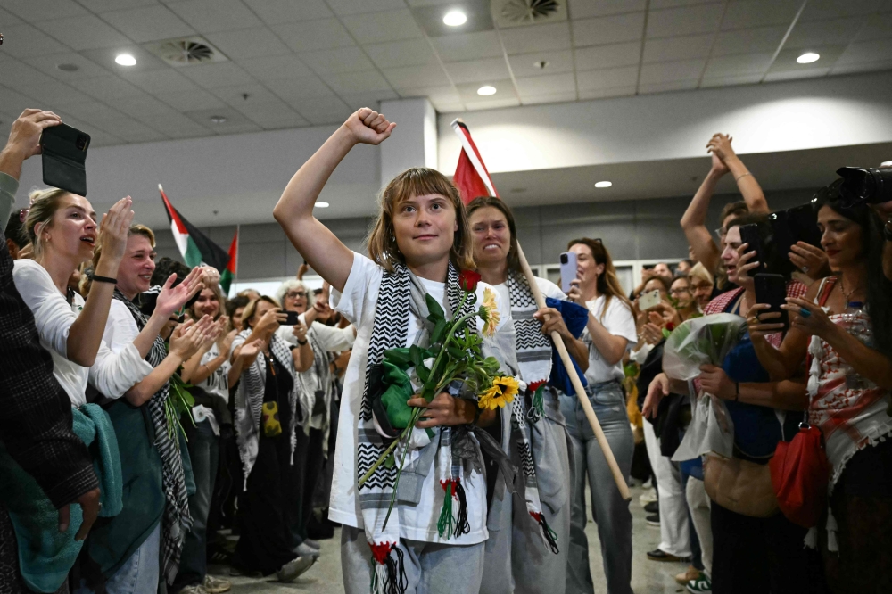 Swedish climate campaigner Greta Thunberg raises her fist, upon arrival alongside activists who were sailing aboard vessels from the Gaza-bound aid flotilla before being stopped and detained by Israeli forces, greeted by a crowd of supporters, at the arrivals area of Athens International Airport on October 6, 2025. (Photo by Aris Messinis / AFP)