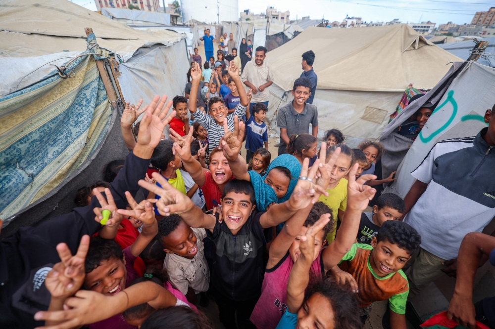 Palestinian children celebrate at a camp for displaced people in Nuseirat in the central Gaza Strip on October 9, 2025, following news of a new peace deal. (Photo by Eyad Baba / AFP)
