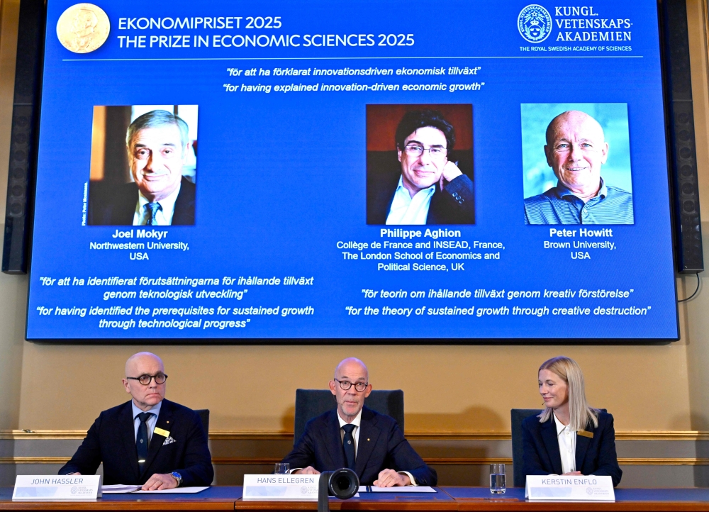 (L-R) John Hassler, Chair of the Committee for the Prize in Economic Science in Memory of Alfred Nobel, the Secretary General of the Royal Swedish Academy of Sciences Hans Ellegren and Kerstin Enflo, member of the Committee for the Prize in Economic Sciences in Memory of Alfred Nobel sit in front of a screen displaying the portraits of the 2025 prize winners. (Photo by Anders Wiklund / TT NEWS AGENCY / AFP) 