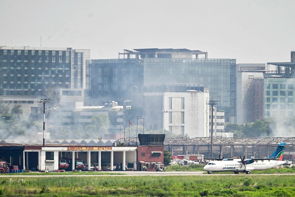 An aircraft prepares to take off as smoke rises from the fire-damaged cargo terminal of Hazrat Shahjalal International Airport in Dhaka on October 19, 2025, a day after the blaze. Photo by Munir UZ ZAMAN / AFP