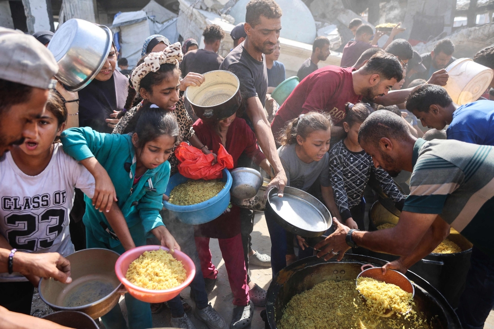 Displaced Palestinians gather to receive food portions outside the damaged Imam al Shafi'i Mosque, where families have taken shelter, in the Zeitoun neighbourhood of Gaza City on October 23, 2025. (Photo by Omar Al-Qattaa / AFP)