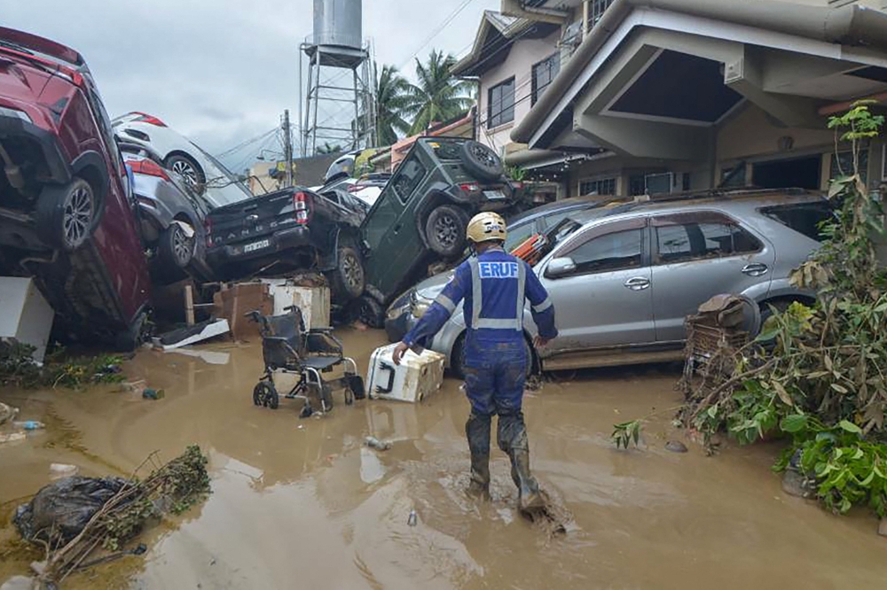 A rescuer walks past piled up cars washed away by floods at the height of Typhoon Kalmaegi in a subdivision of Cebu City in the central Philippines on November 4, 2025. Photo by Alan Tangcawan / AFP