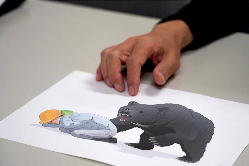 This screen grab from AFPTV video footage taken on October 26, 2025 shows Akita University Hospital's Professor of Emergency and Critical Medicine Hajime Nakae showing a bear attack safety illustration in Akita. (Photo by Caroline Gardin / AFPTV / AFP)