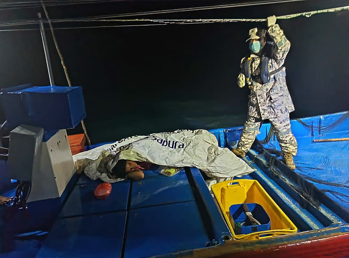 This handout picture taken and released by the Malaysian Maritime Enforcement Agency (MMEA) on November 9, 2025 shows a MMEA staff member checking on a survivor rescued by a fishing boat during a search and rescue operation off the coast of Langkawi, after a boat carrying migrants from Myanmar capsized near the Malaysia-Thailand border. (Photo by Handout / MALAYSIAN MARITIME ENFORCEMENT AGENCY / AFP)