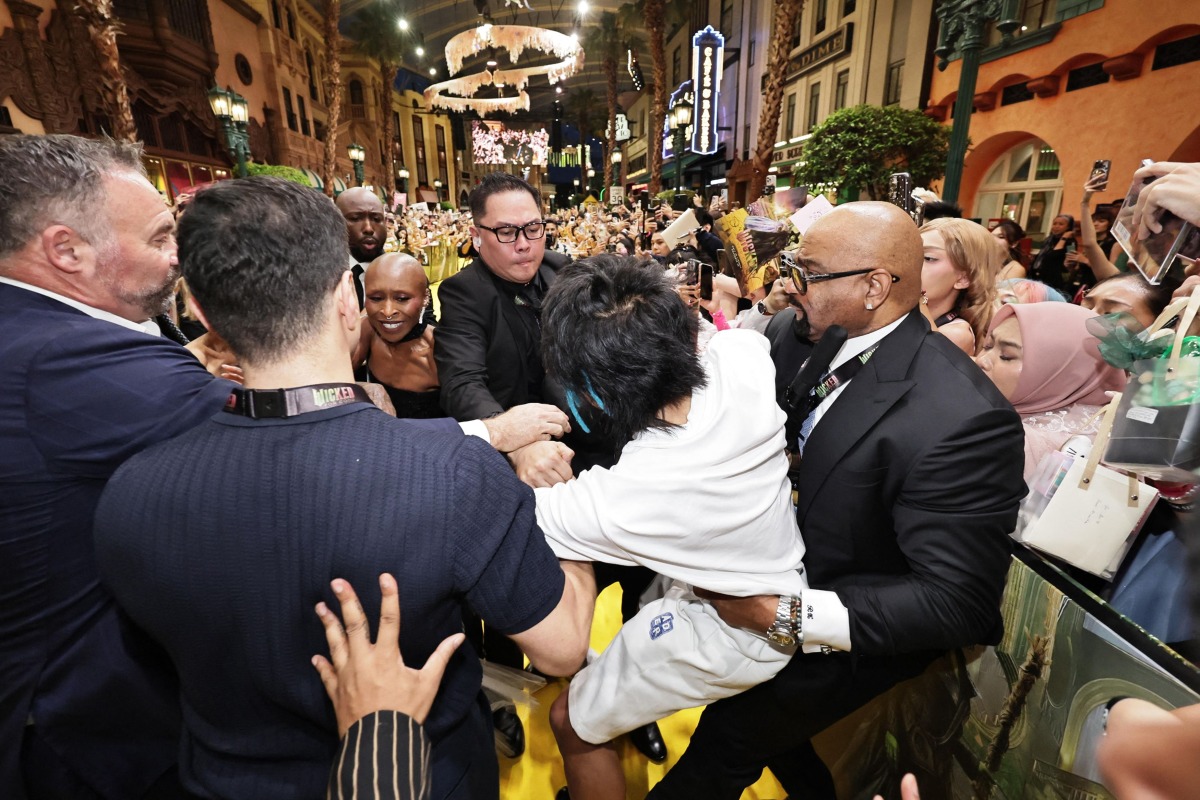 This picture by The Straits Times taken November 13, 2025 and provided on November 14 shows a man (C) accused of attacking pop star Ariana Grande being grabbed by security guards as co-star Cynthia Erivo (3rd L) reacts at the premiere of their film 