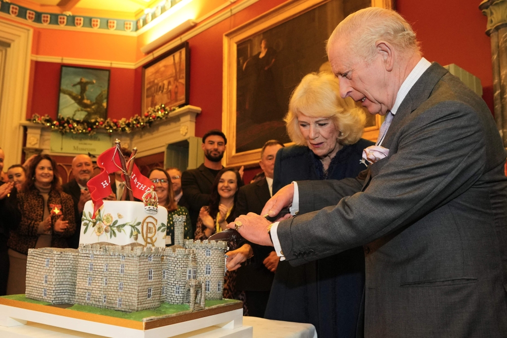 Britain's King Charles III and Britain's Queen Camilla cut into a castle-styled cake at a celebratory reception to mark the 200th anniversary of Cyfarthfa Castle during a visit to the South Wales town of Merthyr Tydfil on November 14, 2025, on the King's 77th birthday. Photo by Kin Cheung /  AFP