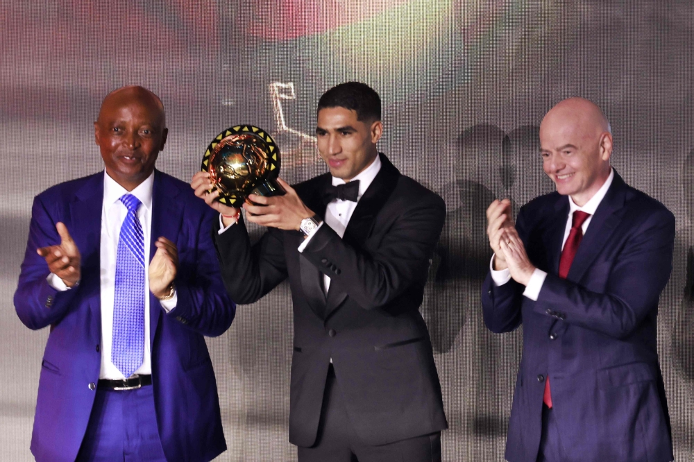Paris Saint-Germain's Moroccan defender Achraf Hakimi (C) holds his Africa Player of the Year award next to CAF President Patrice Motsepe (L) and FIFA President Gianni Infantino (R) during the 2025 Confederation of African Football (CAF) Awards in Sale, Morocco on November 19, 2025. Photo by Abdel Majid Bziouat / AFP