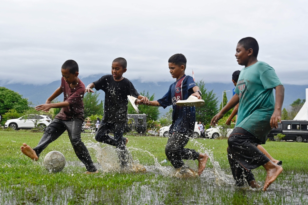 Children play football in a flooded field following rain in Jantho, Aceh province on November 24, 2025. (Photo by Chaideer Mahyuddin / AFP)