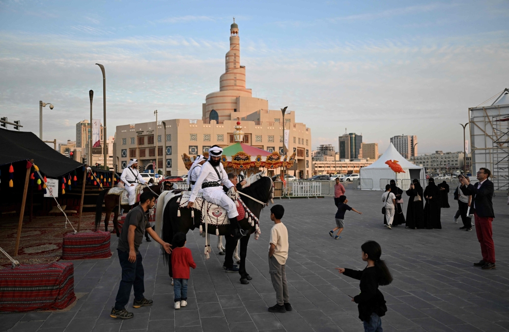 Children and passersby stop to watch men in traditional garb on horseback at the historic Souq Waqif in Qatar on November 26, 2025. (Photo by Mahmud Hams / AFP)