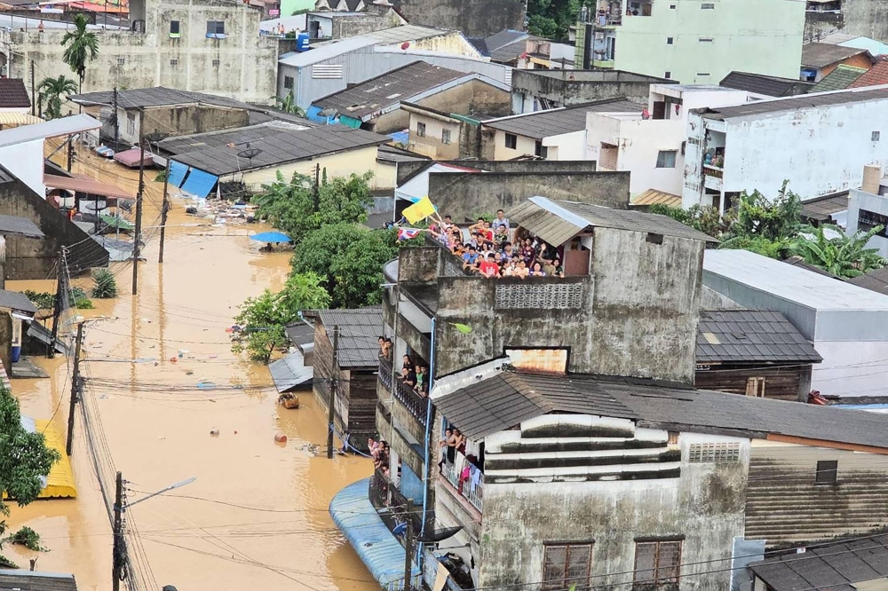 This handout photo taken and released by the Royal Thai Navy on November 26, 2025 shows people looking out from residential buildings surrounded by flood waters in Hat Yai. (Photo by Handout / Royal Thai Navy / AFP) 