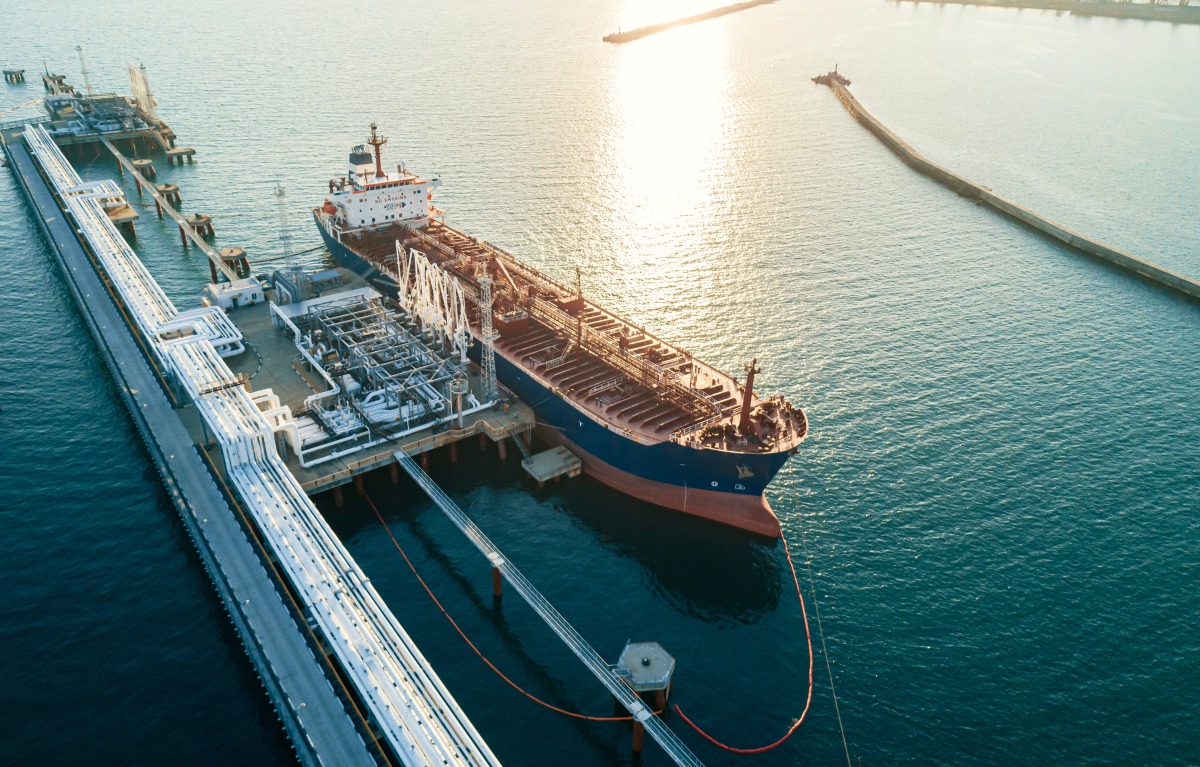 An aerial view of a large oil tanker docked at a pier in the port in process of loading.