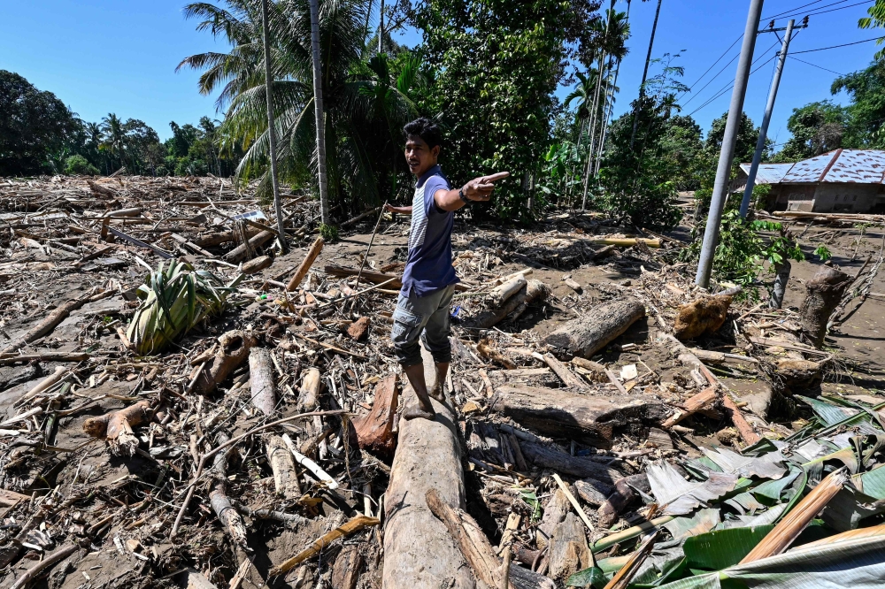A man walks across mud and debris in a flood affected area in Meureudu, Pidie Jaya district in Indonesia's Aceh province on November 30, 2025. (Photo by Chaideer Mahyuddin / AFP)