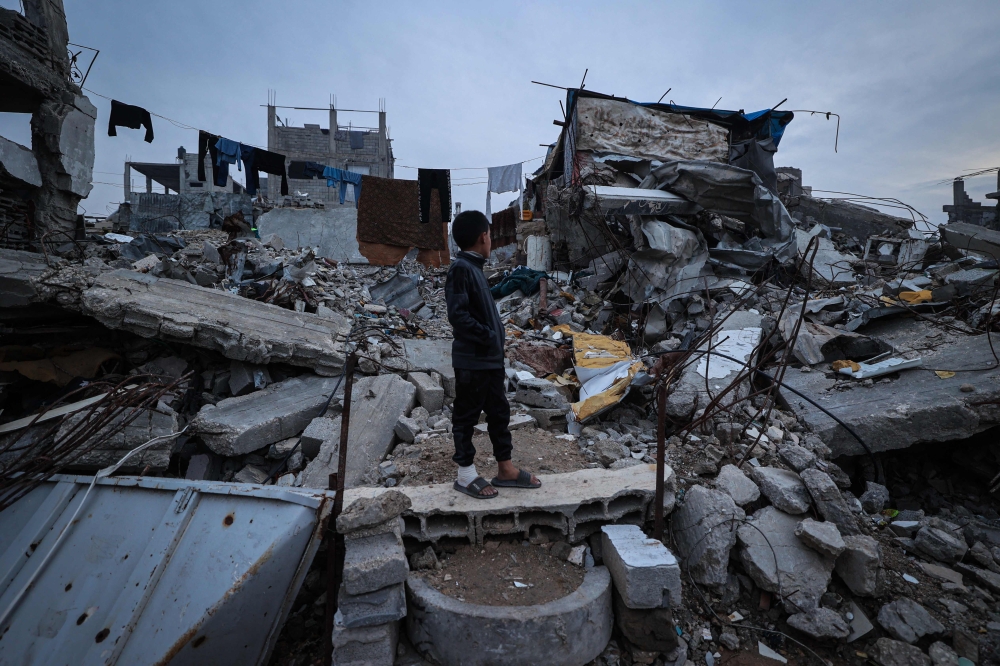 A displaced Palestinian boy stands on the ruins of destroyed buildings in the Bureij refugee camp, in the central Gaza Strip, on November 29, 2025. (Photo by Eyad Baba / AFP)