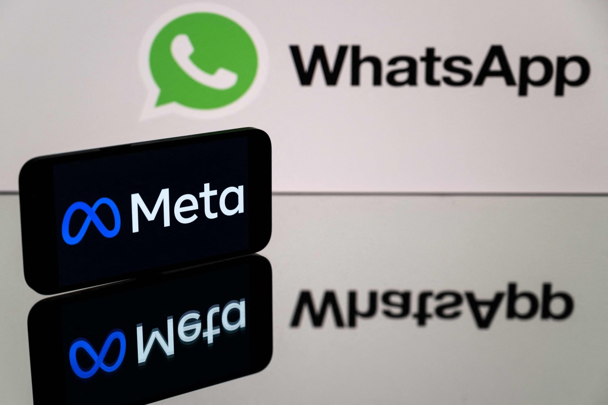 This photograph taken on January 12, 2023 in Toulouse, southwestern France shows a smartphone and a computer screen displaying the logos of WhatsApp app and its parent company Meta. Photo by Lionel BONAVENTURE / AFP