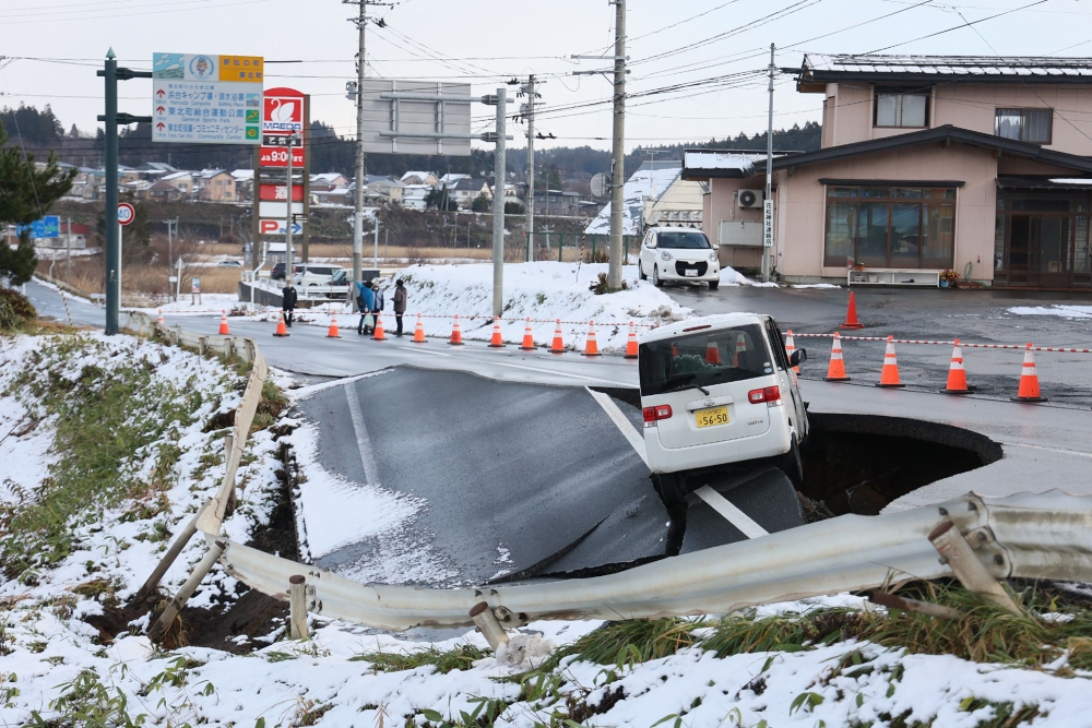 A vehicle rests on the edge of a collapsed road in Tohoku town in Aomori Prefecture on December 9, 2025, following a 7.5 magnitude earthquake off northern Japan. A big quake off northern Japan left at least 30 injured, authorities said on December 9, damaging roads and leaving thousands without power in freezing temperatures. (Photo by JIJI Press / AFP) 