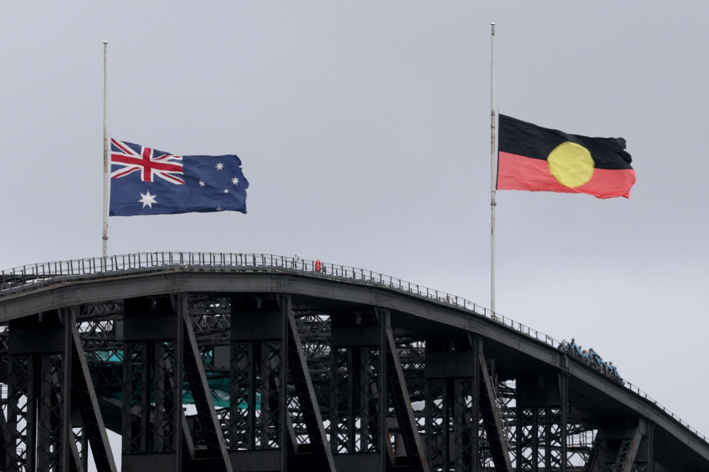 The Australian and Aboriginal flags fly at half-mast on the Sydney Harbour Bridge in the aftermath of the Bondi Beach shootings, in Sydney on December 15, 2025. (Photo by David Gray / AFP)