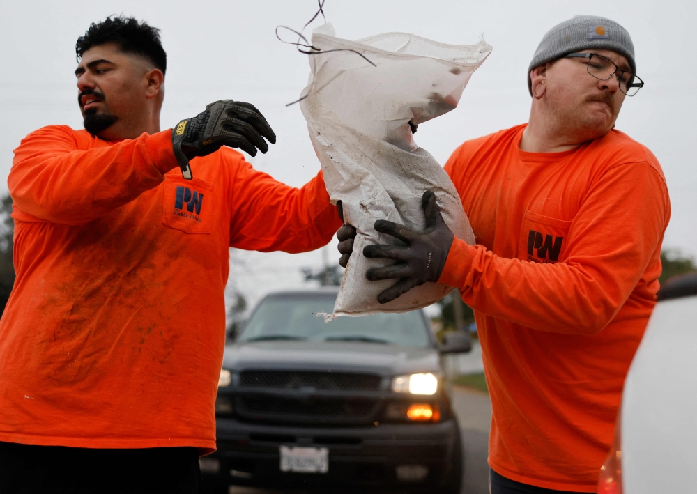 Los Angeles County workers load sandbags for a resident, near the Eaton Fire burn zone, in preparation for a strong atmospheric river storm arriving today to the region on December 23, 2025 in Altadena, California. Photo by Mario Tama/Getty Images/AFP 