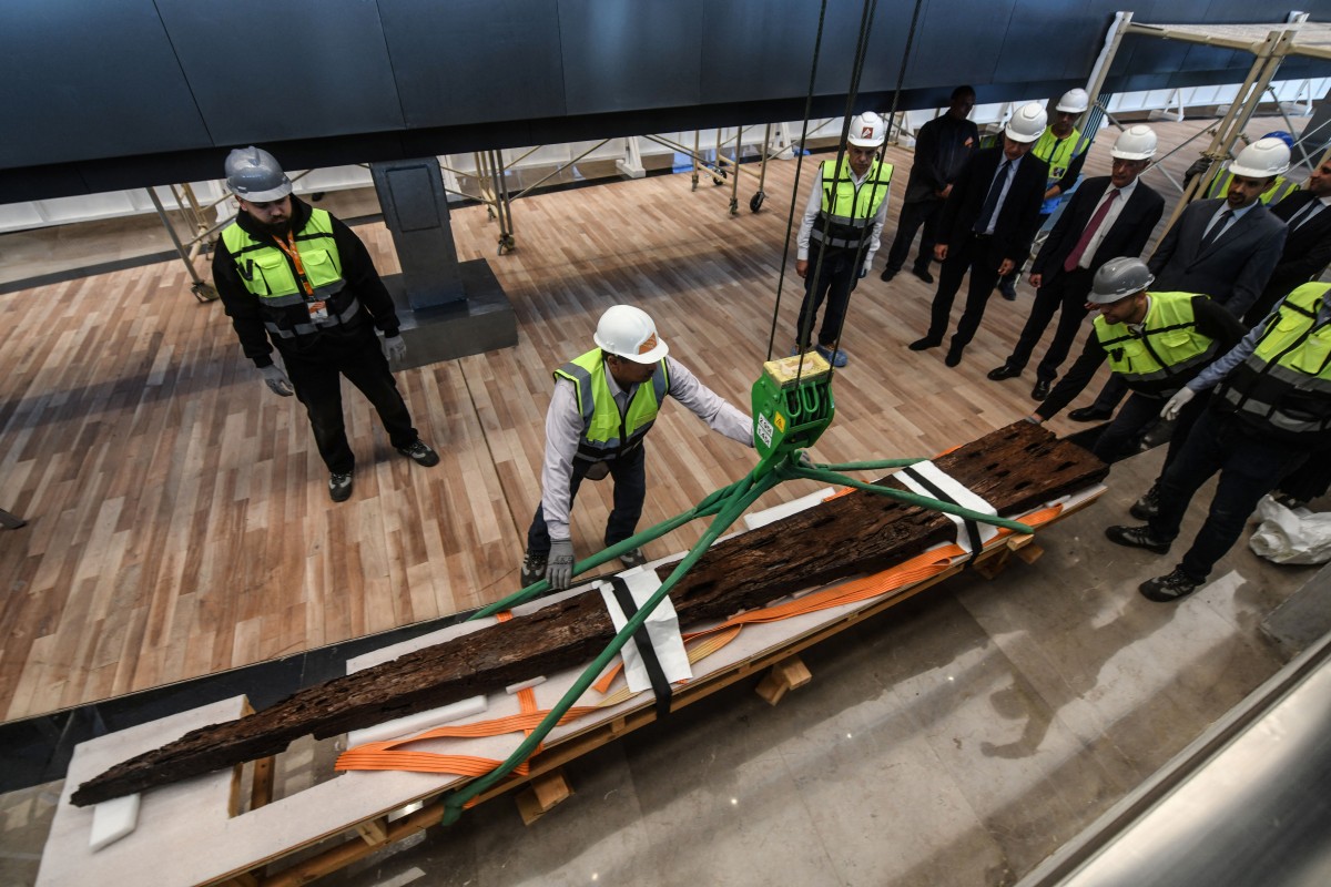 Museum employees install antique wooden planks from King Khufu’s second boat onto a metal structure at the Grand Egyptian Museum in Giza, on the outskirts of Cairo, on December 23, 2025. Photo by Ahmed Hasan / AFP