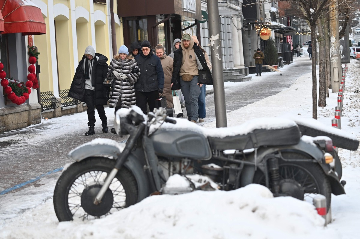 Passers-by walk past a snow-covered motorcycle in the center of Kyiv on January 10, 2026. (Photo by Sergei SUPINSKY / AFP)