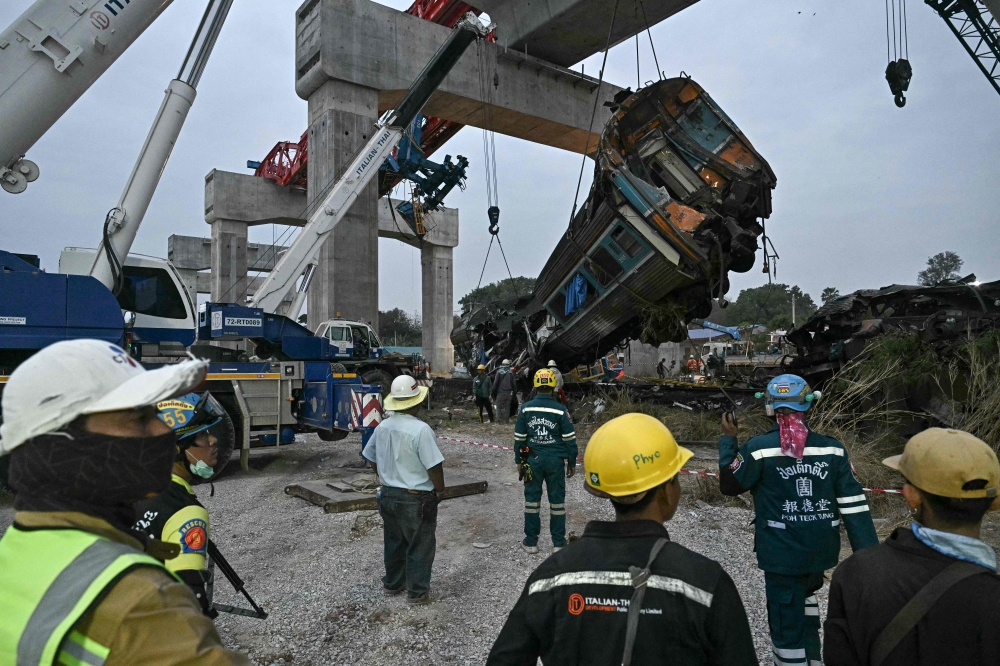 Recovery workers watch as a carriage of a train that crashed when a construction crane collapsed is lifted off the tracks in Thailand's Nakhon Ratchasima province on January 14, 2026. (Photo by Lillian Suwanrumpha / AFP)
 