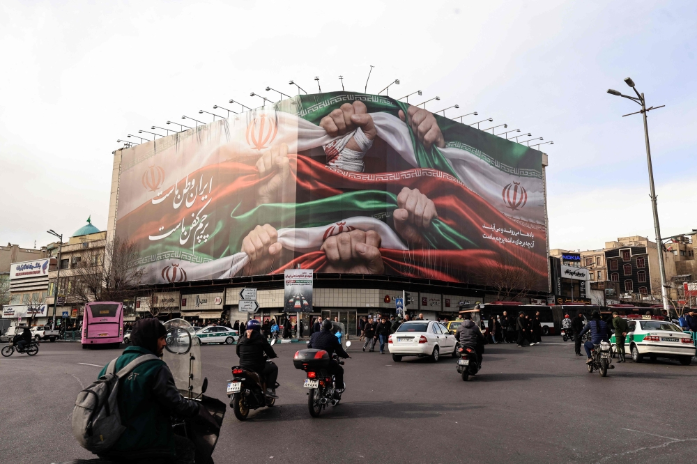 Vehicles pass by a large patriotic banner depicting the Iranian flag in Tehran on January 14, 2026. (Photo by Atta Kenare / AFP)
