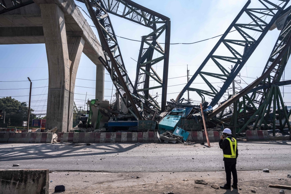 A recovery worker stands near the site of a construction crane collapse onto a highway in Samut Sakhon on the outskirts of Bangkok on January 15, 2026. (Photo by Chanakarn Laosarakham / AFP)
