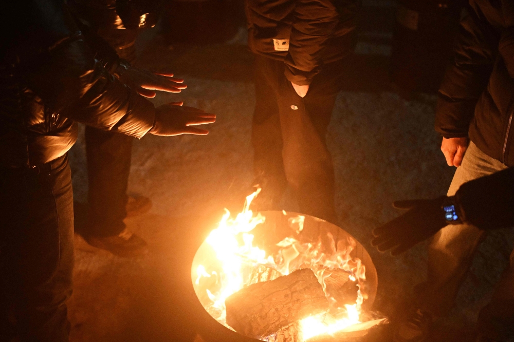 Local residents gather around a bonfire to keep warm as many apartments remain without heating in Kyiv on January 18, 2026. (Photo by Sergei Gapon / AFP)