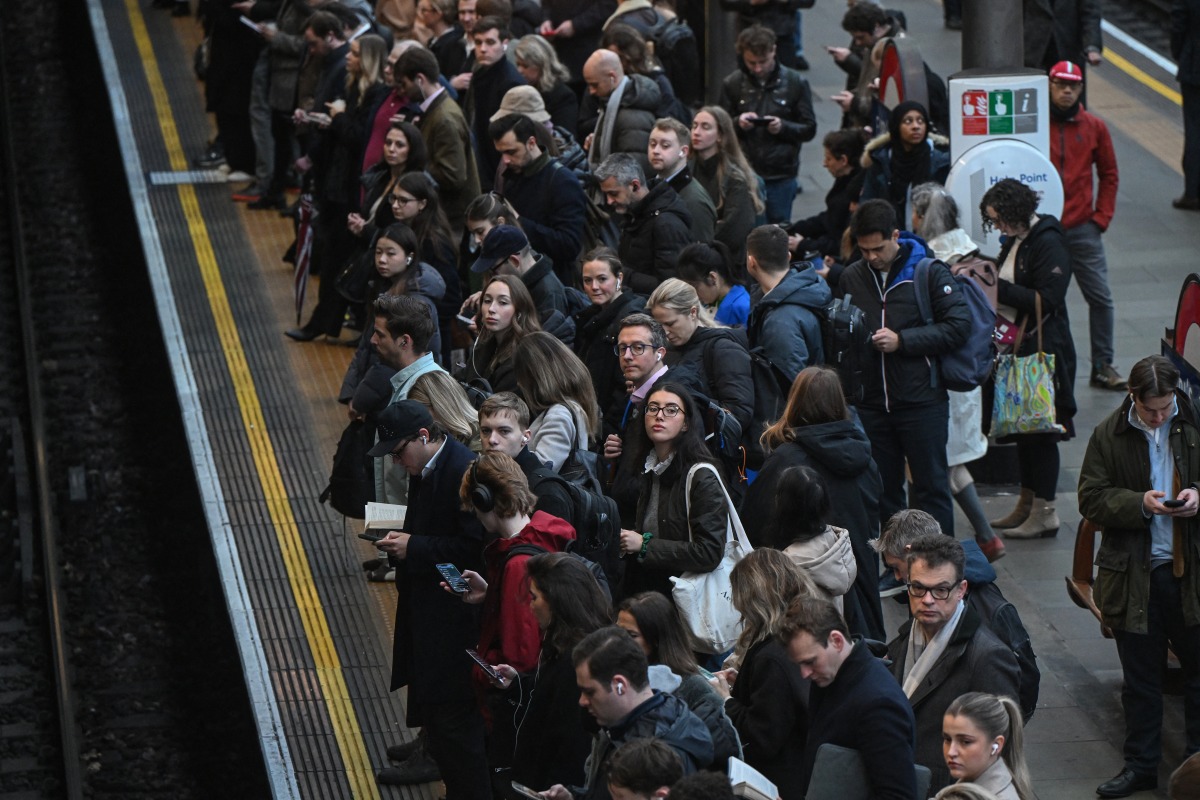 Commuters wait for a train on the platform at Earls Court Tube station in London on January 15, 2026. Photo by JUSTIN TALLIS / AFP