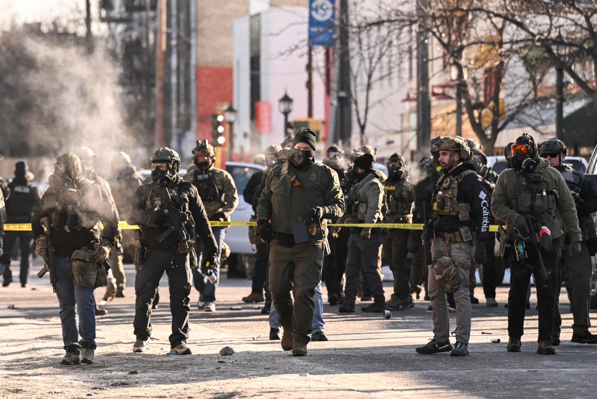 Federal agents stand near police tape as demonstators gather near the site of where state and local authorities say a man was shot by federal agents earlier in the morning in Minneapolis, Minnesota, on January 24, 2026. (Photo by ROBERTO SCHMIDT / AFP)