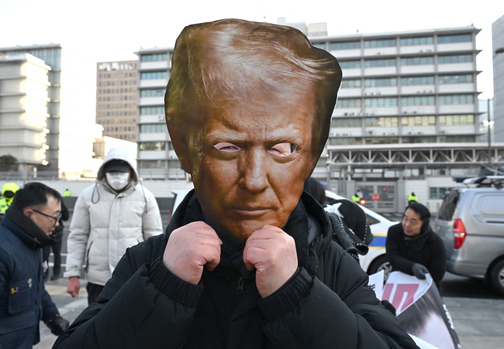 A protester wears a mask of US President Donald Trump during a rally condemning Trump's plans to raise tariffs in front of the US embassy in Seoul on January 27, 2026. (Photo by Jung Yeon-je / AFP)