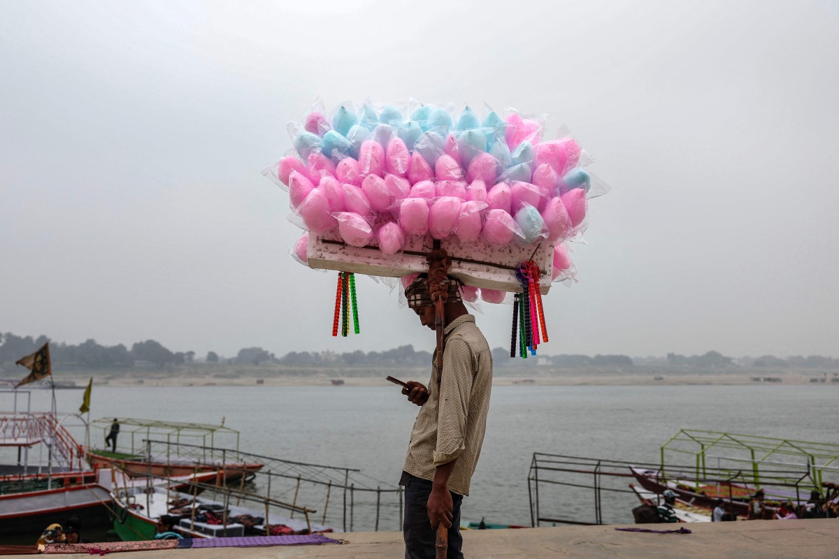 A cotton candy vendor uses his mobile phone as he waits for customers along the banks of the river Ganges in Varanasi on January 29, 2026. (Photo by Niharika KULKARNI / AFP)