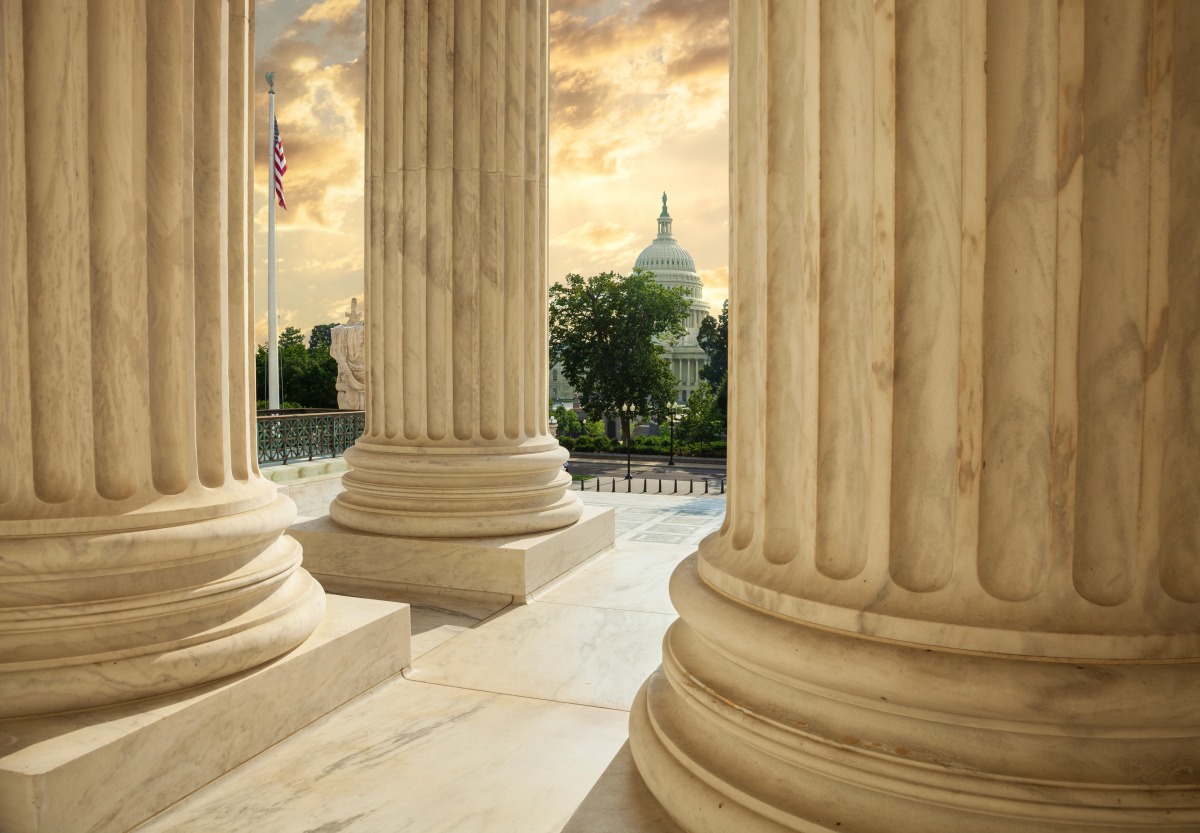 US Capitol building viewed between columns of the Supreme Court at sunset.