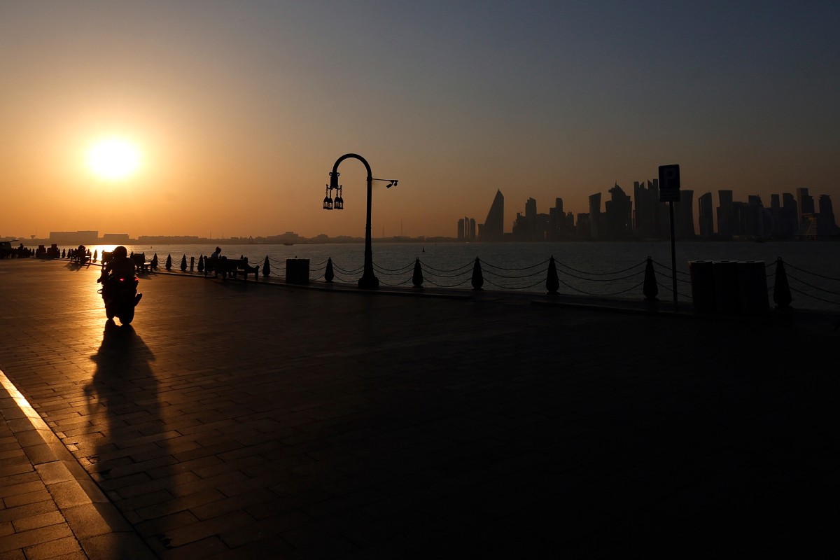 A man is silhouetted by the setting sun as he rides his motorcycle in Doha's Mina district on February 26, 2026. (Photo by Karim Jaafar / AFP)