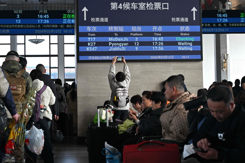 A man takes pictures of a board with a sign for the K27 train bound for Pyongyang as passengers wait for their train at Beijing Railway Station in Beijing on March 12, 2026. The first passenger train service from North Korea to China crossed the border March 12 for the first time in six years, Yonhap News Agency reported. (Photo by Adel Berry/ AFP)
 