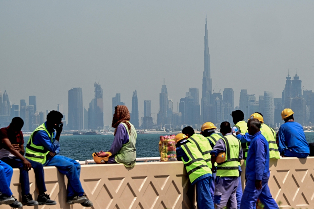 (Files) Workers sit on a wall against the backdrop of the Dubai city skyline on March 11, 2026. (Photo by Giuseppe Cacace / AFP)