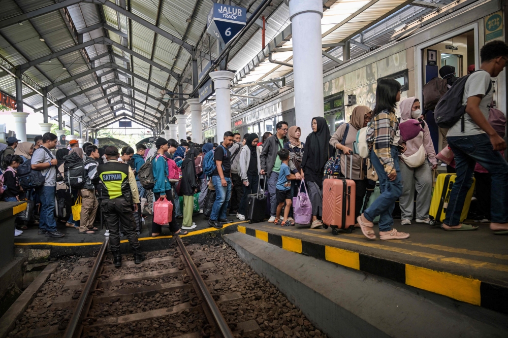 Passengers prepare to board a train to return home ahead of Eid al-Fitr, at Gubeng station in Surabaya on March 17, 2026. (Photo by Juni Kriswanto / AFP)